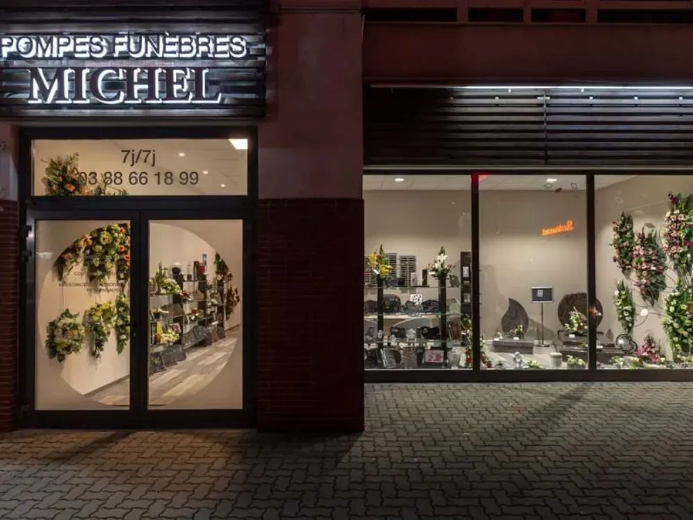 Façade de l'agence Pompes Funèbres Michel éclairée de nuit, avec vitrines.